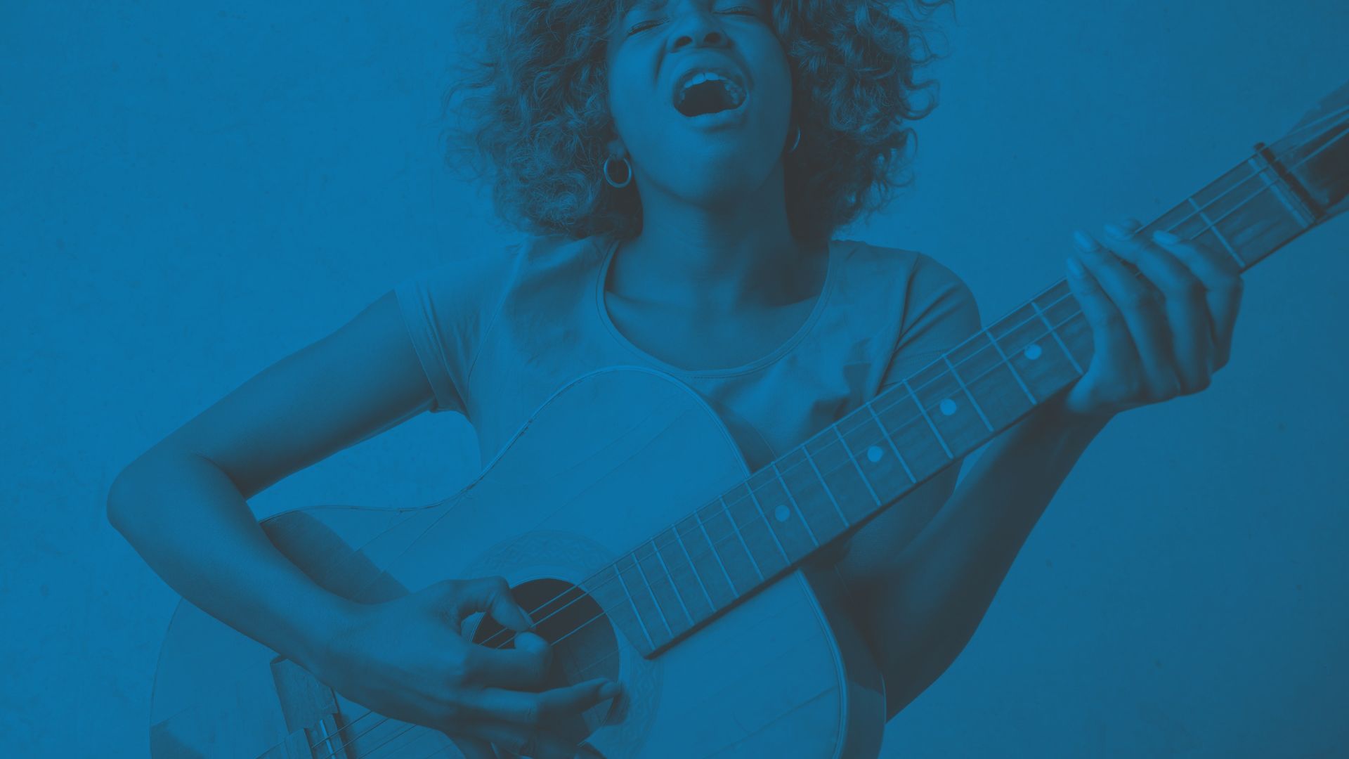 Image of a young woman singing with a guitar - The fund is to support access to music education and music-making opportunities for disadvantaged young people and communities.
